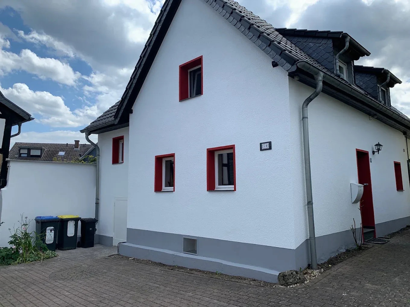 Weiß gestrichenes Haus mit rot lackierten Fensterrahmen und Haustür