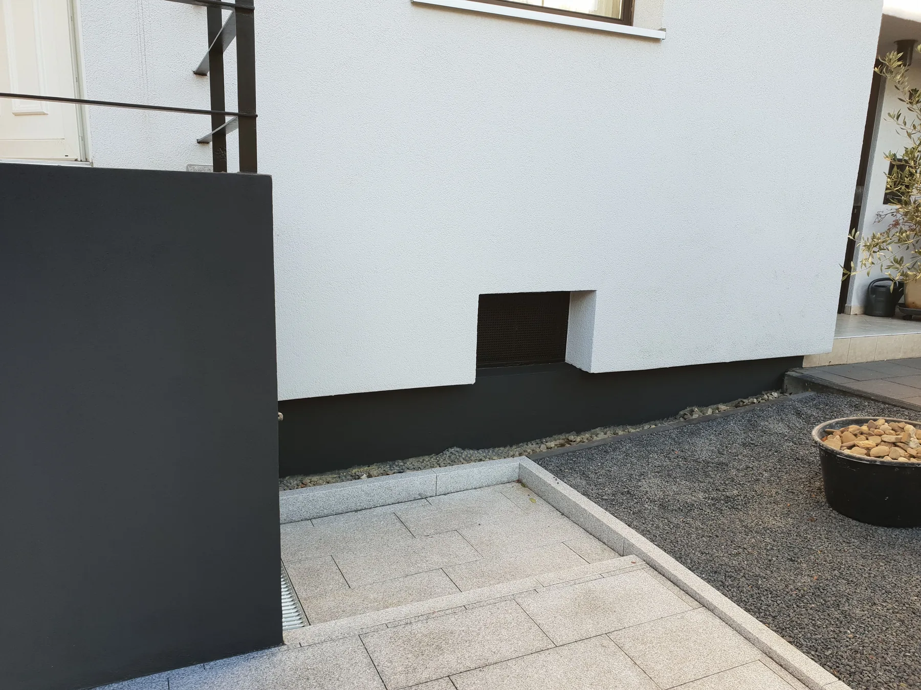 Weiß gestrichene Hauswand mit anthrazitfarbenem Sockel und Mauer
