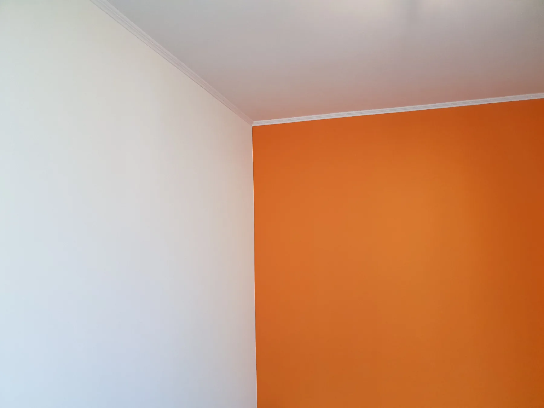 Raumecke mit weißer Wand und leuchtend orangefarbener Akzentwand
