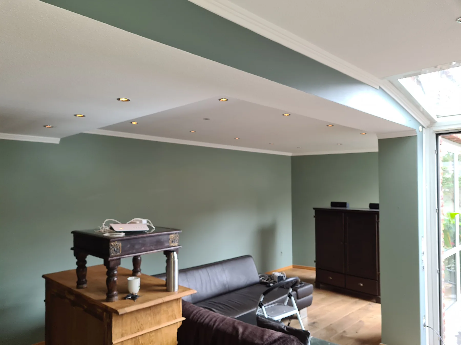 Wohnzimmer mit salbeigrün gestrichenen Wänden und weißer Decke